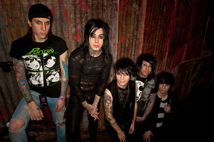 Ex-con rock star and band members posing against a rustic wall, embodying a rebellious rock style and attitude.