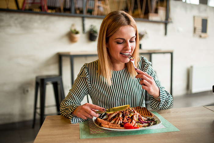 Young woman eating a meal at a cafe, illustrating woman ends up in the ER from anaphylactic shock concept.