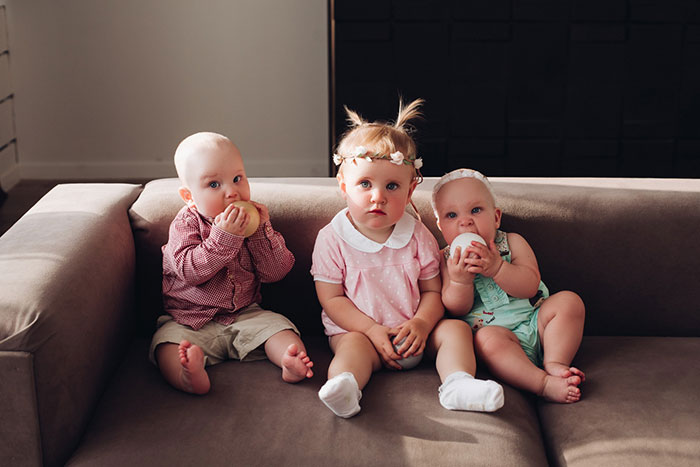 Three babies sitting on a couch, two holding round toys, siblings showing family ties and contrast in lifestyles. Three babies sitting on a couch, two holding round toys, siblings showing family ties and contrast in lifestyles.