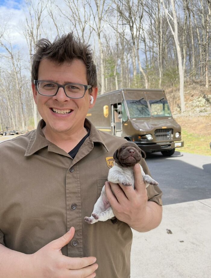 UPS driver smiling while holding an adorable puppy outside with a UPS delivery truck in the background