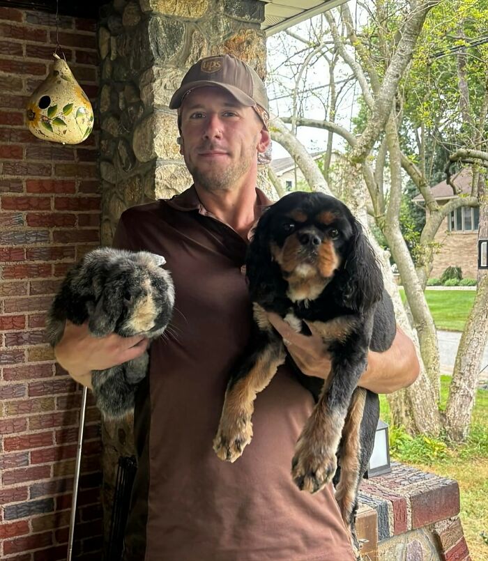 UPS driver holding an adorable dog and a fluffy rabbit outside a house during a pet visit.