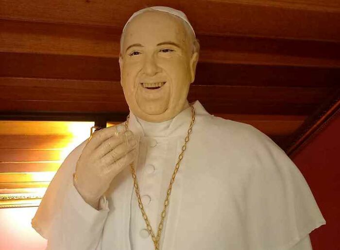 Wax sculpture of a famous figure resembling a pope, with a surprisingly creepy and hilarious expression.