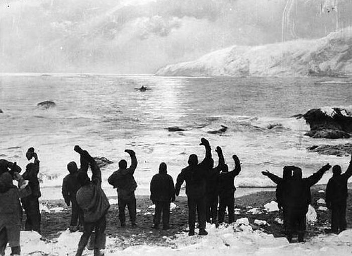 People on a snowy shore waving at a small boat in the sea, showcasing real life more interesting and bizarre than fiction.