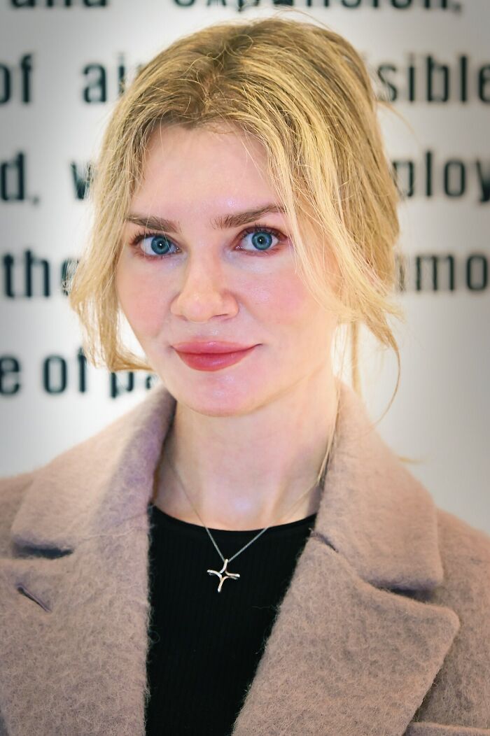 Blonde woman with blue eyes wearing a beige coat and black top, representing famous fraud cases in a professional setting.