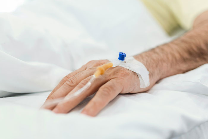 Close-up of a man's hand with IV drip in hospital bed, related to testicular cancer diagnosis and unusual blood test results.