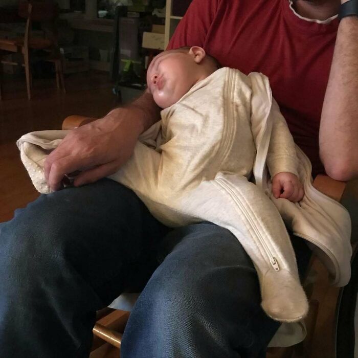 Dad holding a sleeping baby in a relaxed pose, highlighting funny photos revealing the differences between moms and dads.