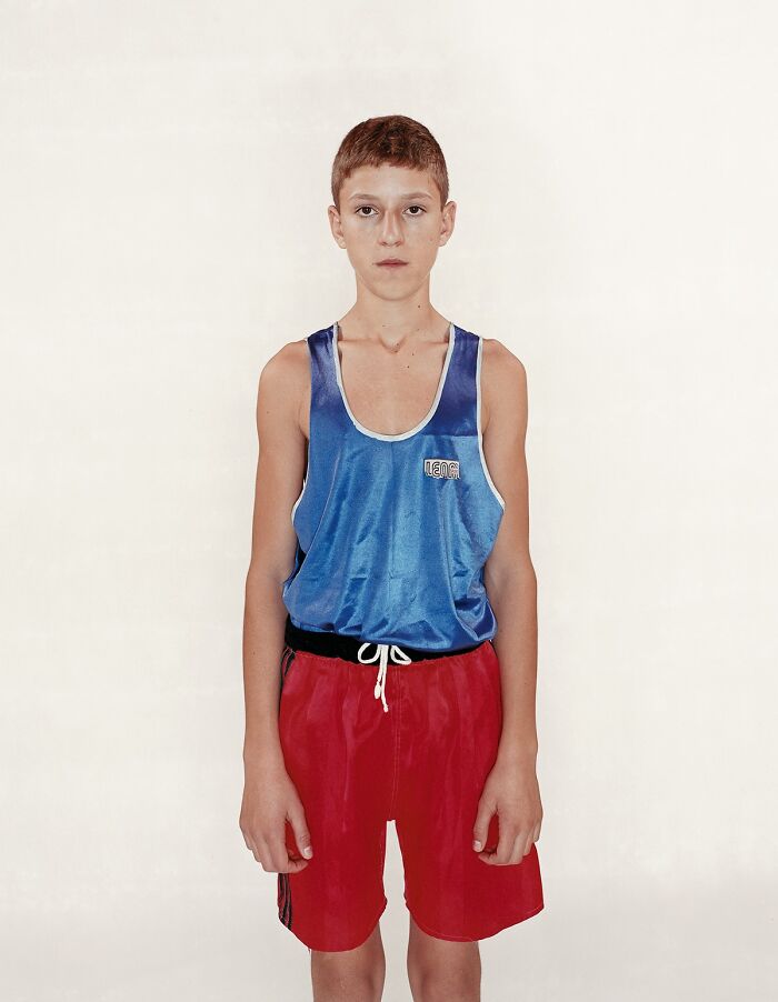 Young boxer wearing blue tank top and red shorts, posing for powerful photographs before their first match.