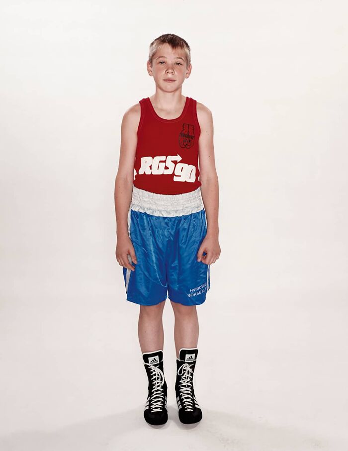 Young boxer wearing red tank top and blue shorts standing before his first match in powerful photographs series.
