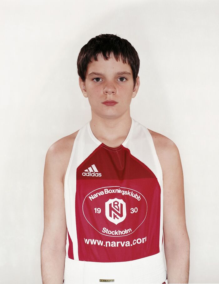 Young boxer wearing red and white gear, standing against a plain background before his first boxing match.