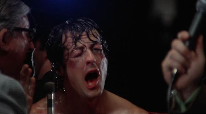 Close-up of a sweaty man shouting into a microphone during an intense scene, illustrating famous movie tropes.