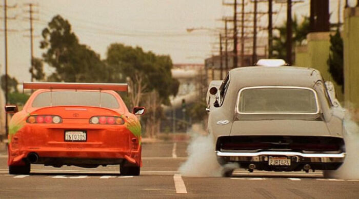 Two cars racing on a street with smoke from tires, illustrating a popular beloved movie tropes scene from a street racing film.