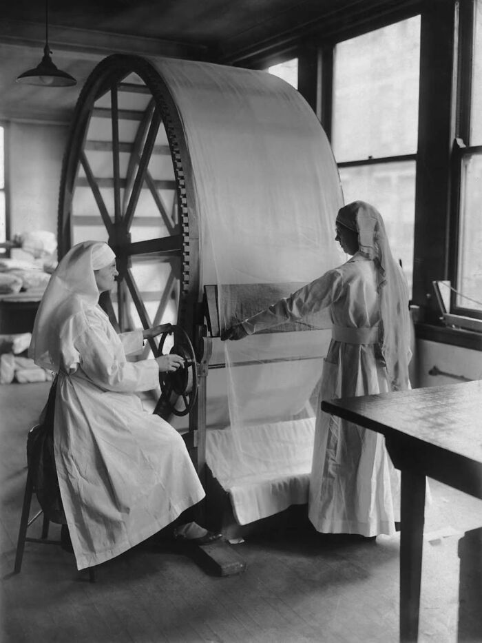 Two nurses operating a large fabric machine in a vintage medical facility, showcasing old-school medical equipment.