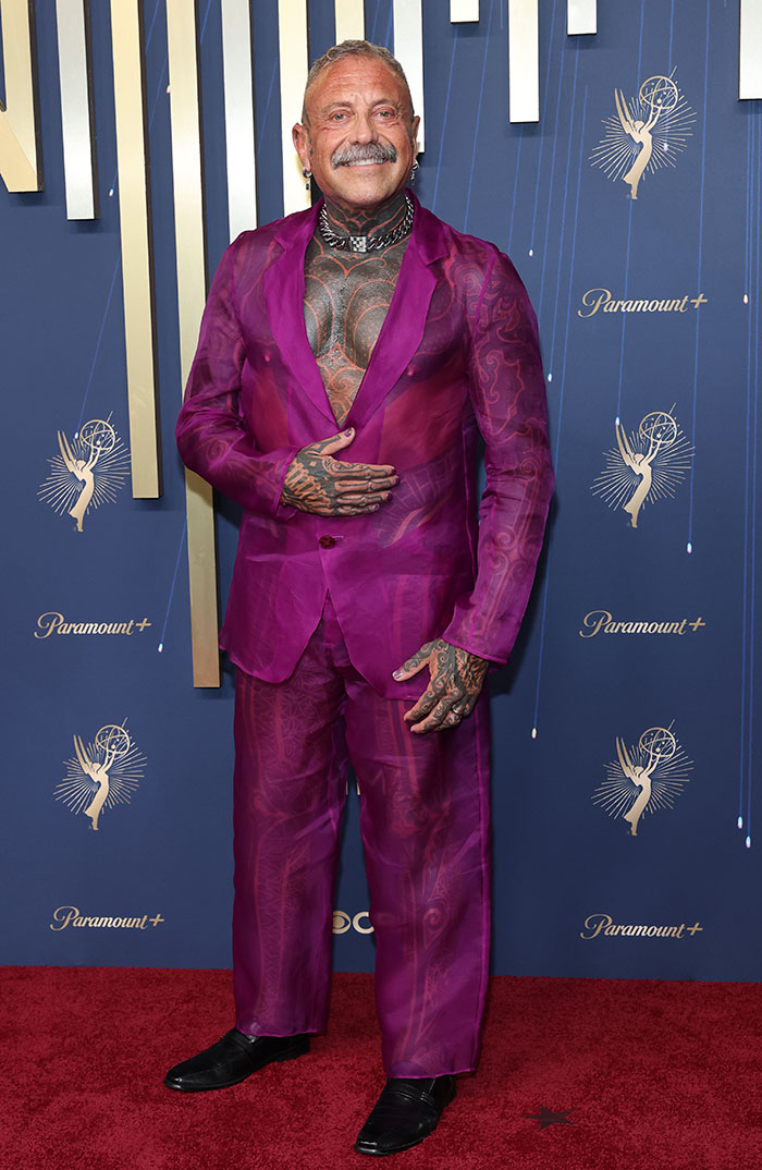 Man with extensive tattoos wearing a sheer purple suit posing on the red carpet at the 2025 Emmys fashion event.
