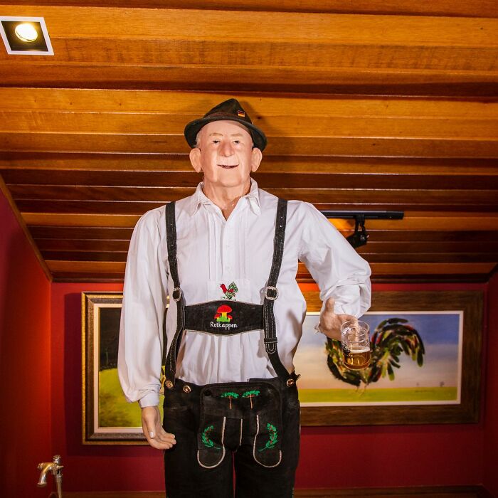 Wax sculpture of a man in traditional attire holding a beer mug, showcasing creepy and hilarious wax art by this artist.