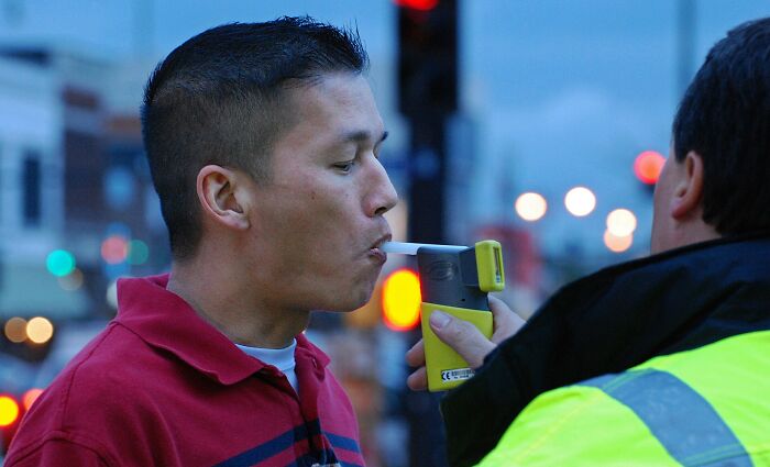Man in red shirt blowing into breathalyzer held by police officer in yellow vest during roadside test showing innocent people blamed by police.