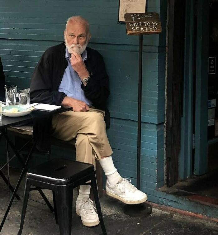Elderly man in casual stylish outfit sitting at outdoor café, embodying cool and stylish grandparents fashion.