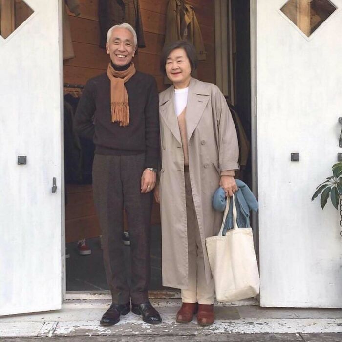 Stylish grandparents standing together, wearing chic outfits with a scarf, trench coat, and casual accessories.