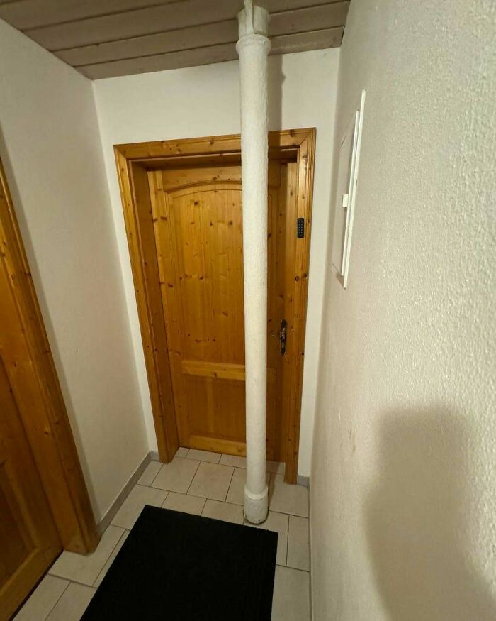 Wooden door blocked by a white construction pipe inside a narrow hallway showing flawed design and poor construction.