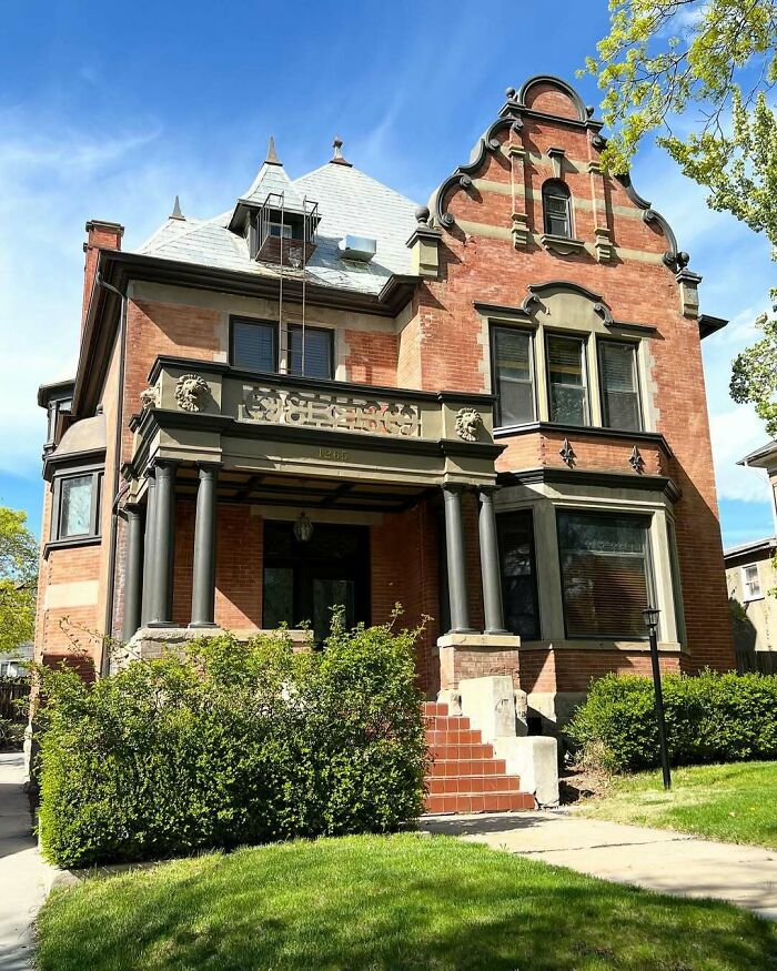 Large charming old home with detailed brickwork, ornate facade, and green lawn under a clear blue sky.