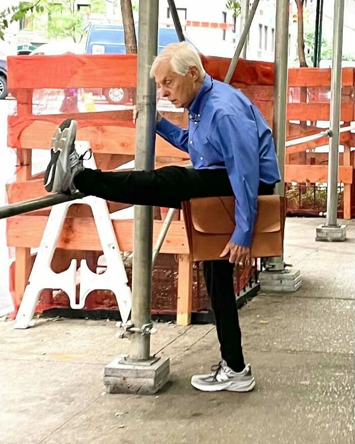 Elderly man in stylish outfit stretching leg outdoors, showcasing cool and fashionable grandparents' confident street style.