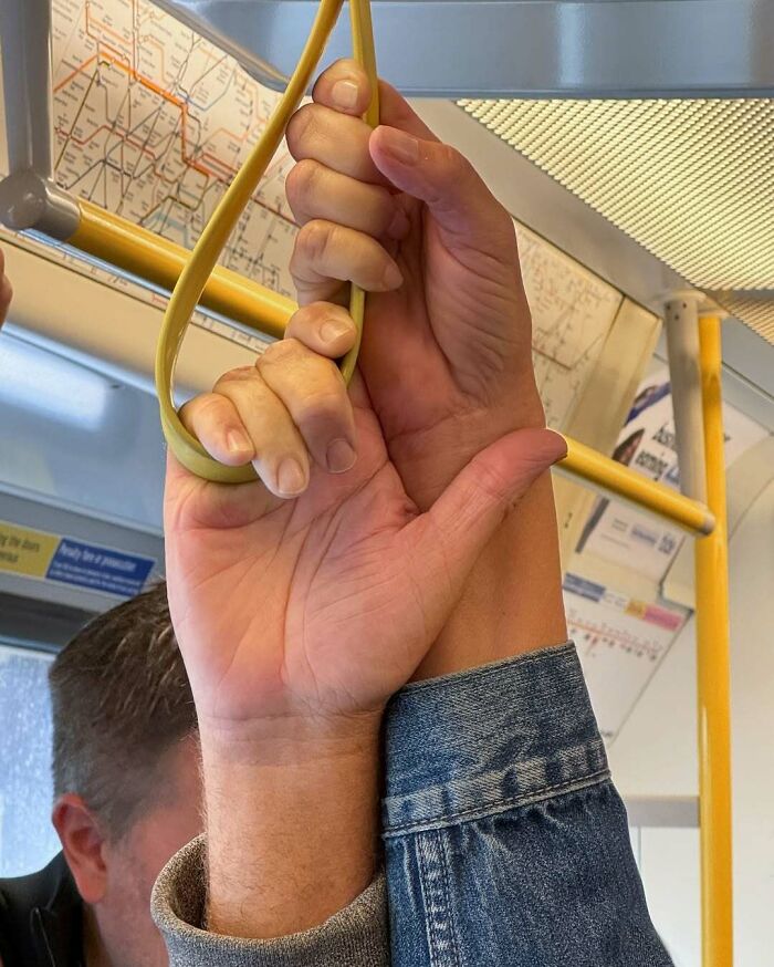 Two people on the New York subway holding onto a yellow strap handle while standing close together.