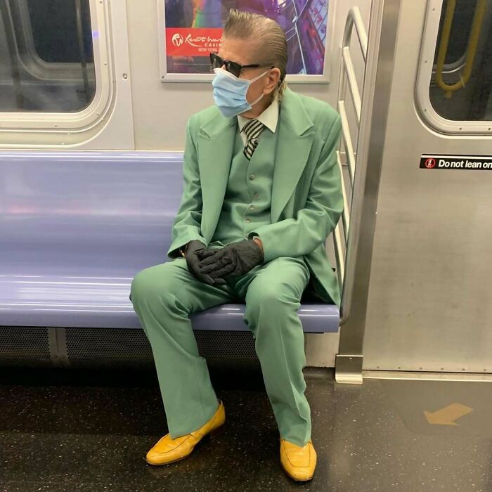 Stylish grandparent wearing a mint green suit, yellow shoes, black gloves, and sunglasses sitting on a subway train.