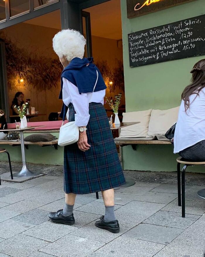 Elderly woman showcasing cool and stylish grandparents fashion walking near a café with classic outfit details.