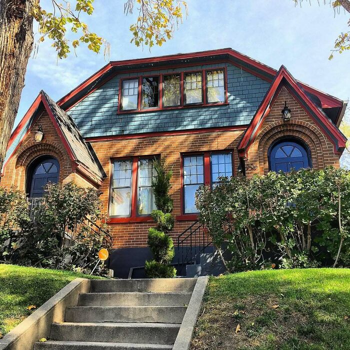 Charming old home with brick facade, red trim, and lush greenery, an adorable and lovely old home perfect for moving in soon.
