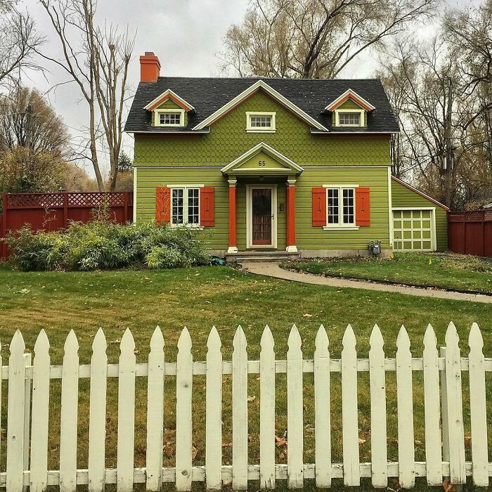 Charming old home with green siding, orange shutters, and a white picket fence in a peaceful neighborhood setting.