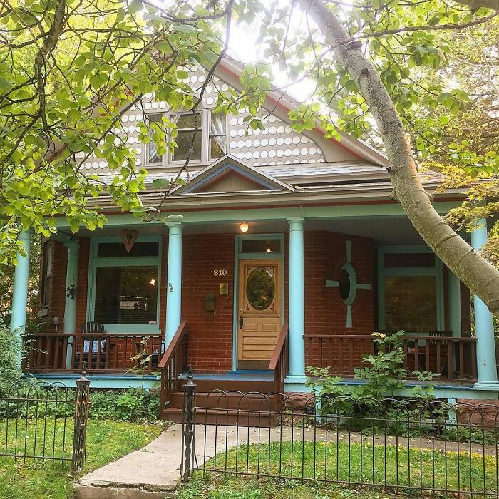 Charming old home with a welcoming porch, turquoise pillars, and lush greenery in a cozy neighborhood setting.