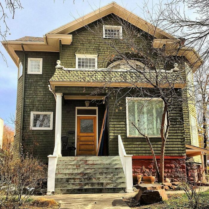 Charming old home with green exterior, wooden door, white columns, and vintage architectural details in a residential neighborhood.