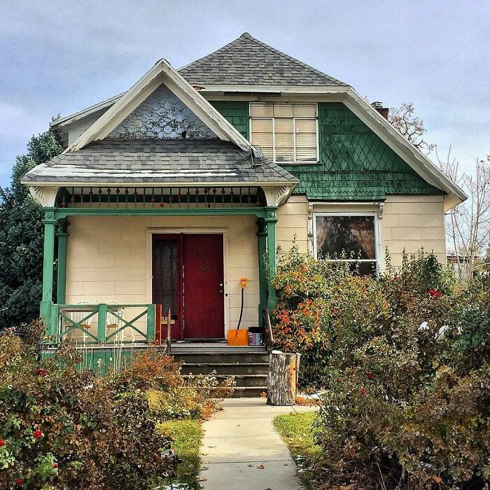 Charming old home with green trim, a red door, and a lush garden path leading to the porch in autumn.