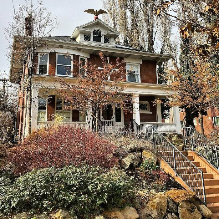 Lovely old home with a brick exterior, wrap-around porch, and autumn trees in a charming residential neighborhood.