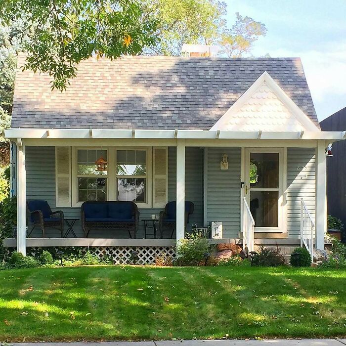 Charming old home with a cozy front porch, outdoor seating, and a well-maintained lawn on a sunny day.