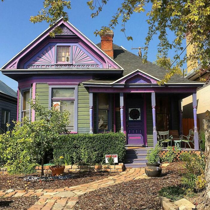 Adorable old home with purple and green exterior, charming porch, and landscaped garden in a sunny neighborhood setting.