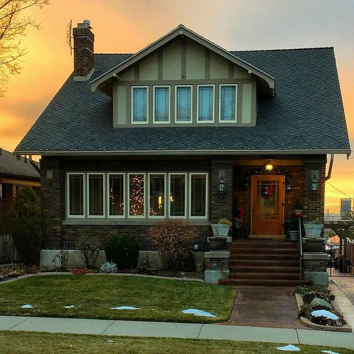 Charming old home with brick exterior and warm sunset, featuring a front porch and well-kept lawn in a residential neighborhood.