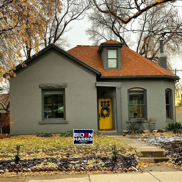 Charming old home with gray exterior, orange roof, and yellow door surrounded by autumn leaves in a residential neighborhood.