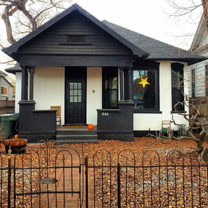 Charming old home with black and white exterior, autumn leaves in yard, and a glowing star decoration in the window.