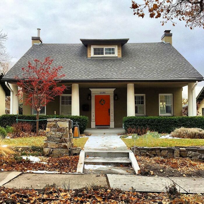 Charming old home with gray roof, bright orange door, and autumn landscaping in a cozy neighborhood setting.