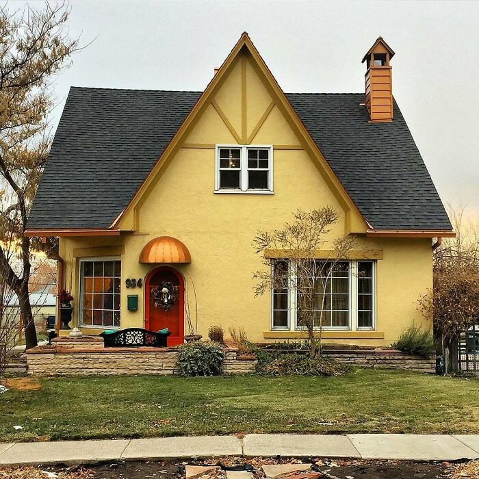 Charming old home with a steep roof and orange door, surrounded by a green lawn and autumn trees.