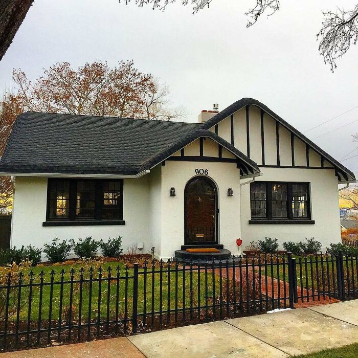 Charming old home with white exterior and black trim, surrounded by a black iron fence and autumn landscaping.