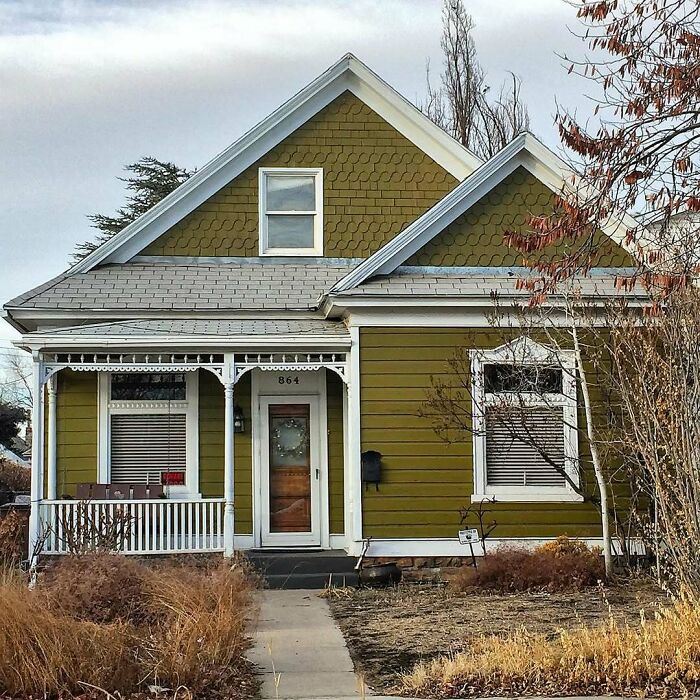 Charming old home with green siding, white trim, and a small porch surrounded by dry grass and trees in late autumn.