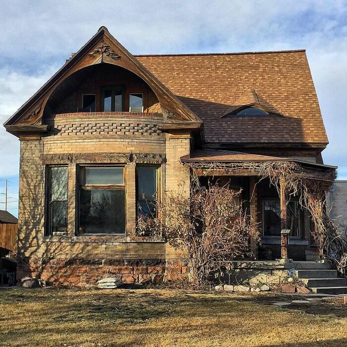 Charming old home with unique architecture, wooden details, and a rustic porch surrounded by dry vines and lawn.