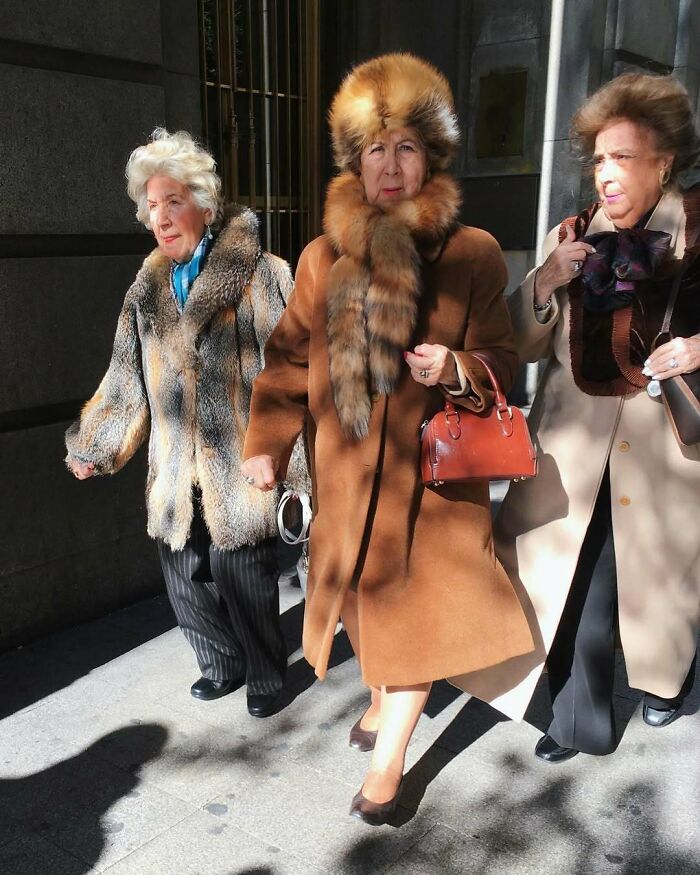 Three stylish grandparents wearing elegant fur and wool coats walking confidently on a city street in winter.
