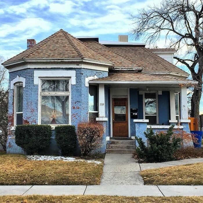 Blue charming old home with worn paint, bushes, and a wooden door in a quiet neighborhood on a clear day.