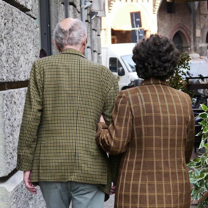 Stylish grandparents walking arm in arm wearing fashionable checkered blazers, showcasing cool and trendy outfits.