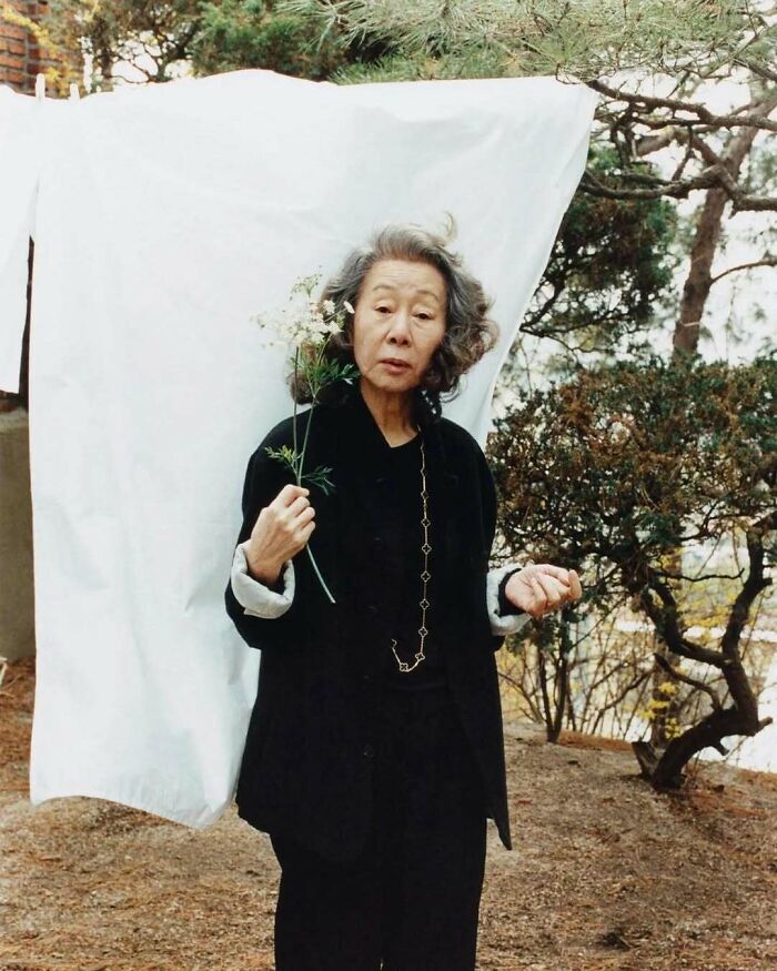 Stylish grandparent in a black outfit holding a flower outdoors, showcasing cool and fashionable senior style.