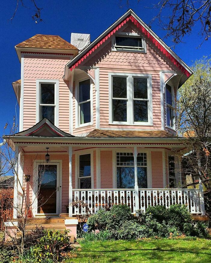Victorian-style old home with pink siding, white trim, and a decorative front porch under a clear blue sky.