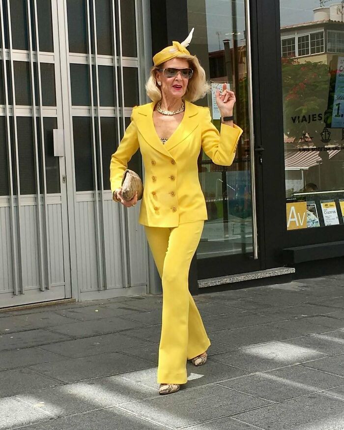 Stylish grandparent in a bright yellow suit and matching hat confidently walking on the street with sunglasses and accessories.