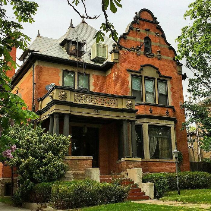 Victorian-style old home with ornate brickwork, large windows, and a lush green front yard surrounded by trees.